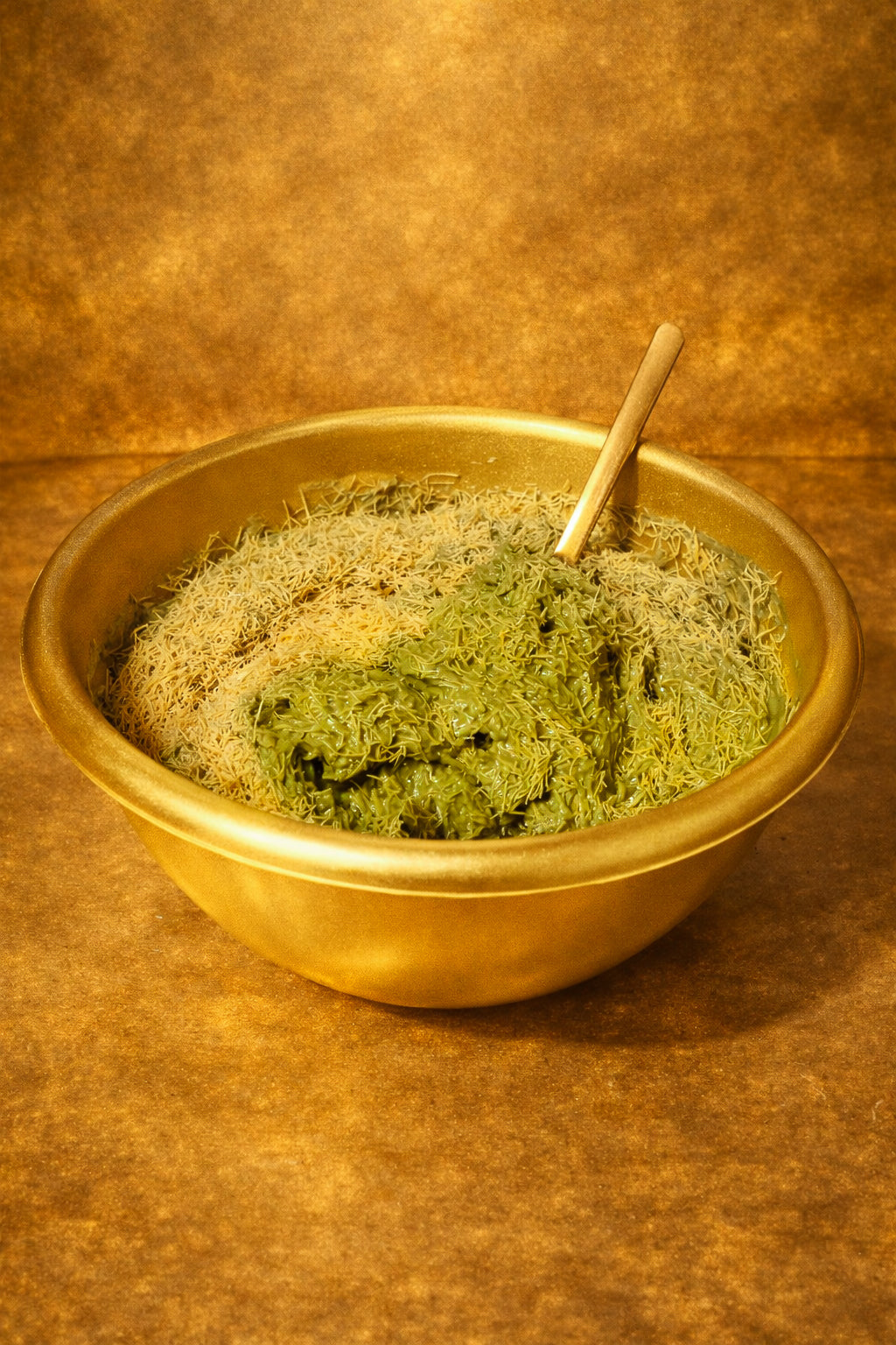 Goldene Schale mit fein gehacktem Kadayif-Teig und cremiger Pistazienfüllung, stilvoll angerichtet auf warmem goldenen Hintergrund mit Holzlöffel